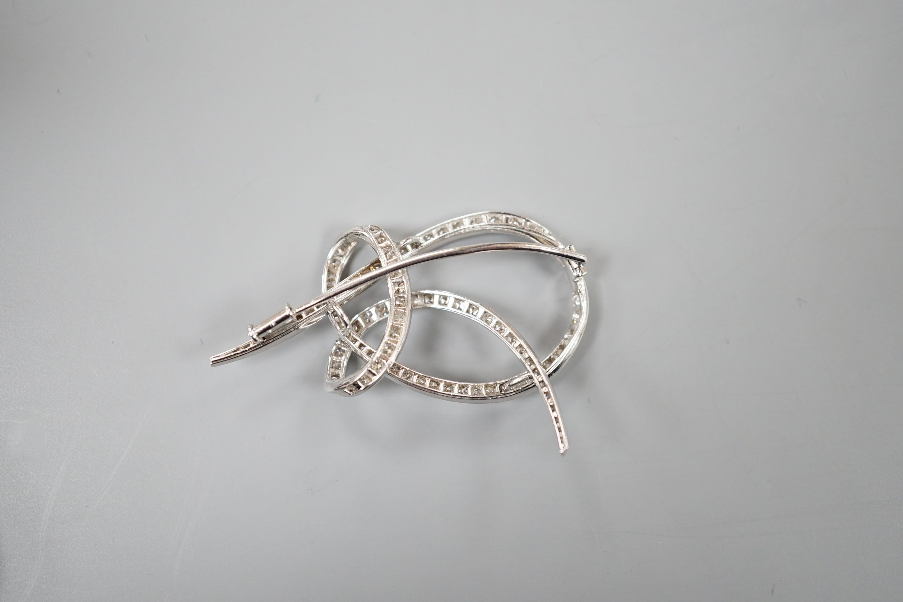 A white metal and diamond cluster set scroll brooch, 52mm, gross weight 14 grams.